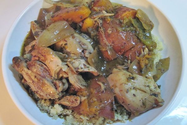 Spiced chicken and vegetables over grains in a white bowl