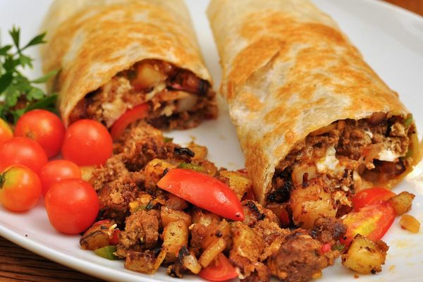 Two breakfast burritos cut open with tomatoes on the side